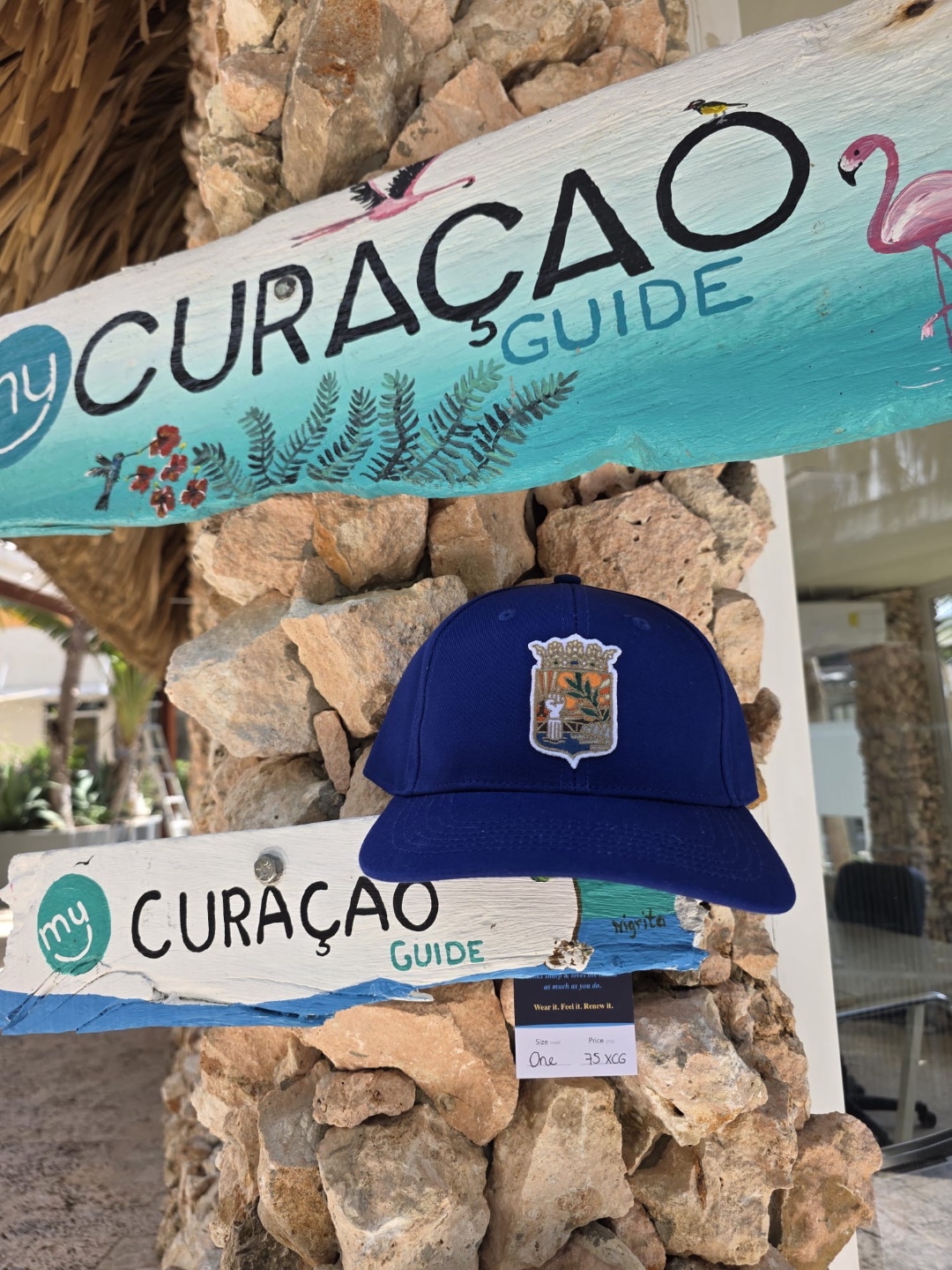 ReNova navy cap met Curaçao wapenschild bij het Curaçao Guide bord